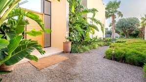Un bâtiment moderne doté d’une grande porte en verre, entouré d’une végétation luxuriante comprenant des bananiers et un palmier.