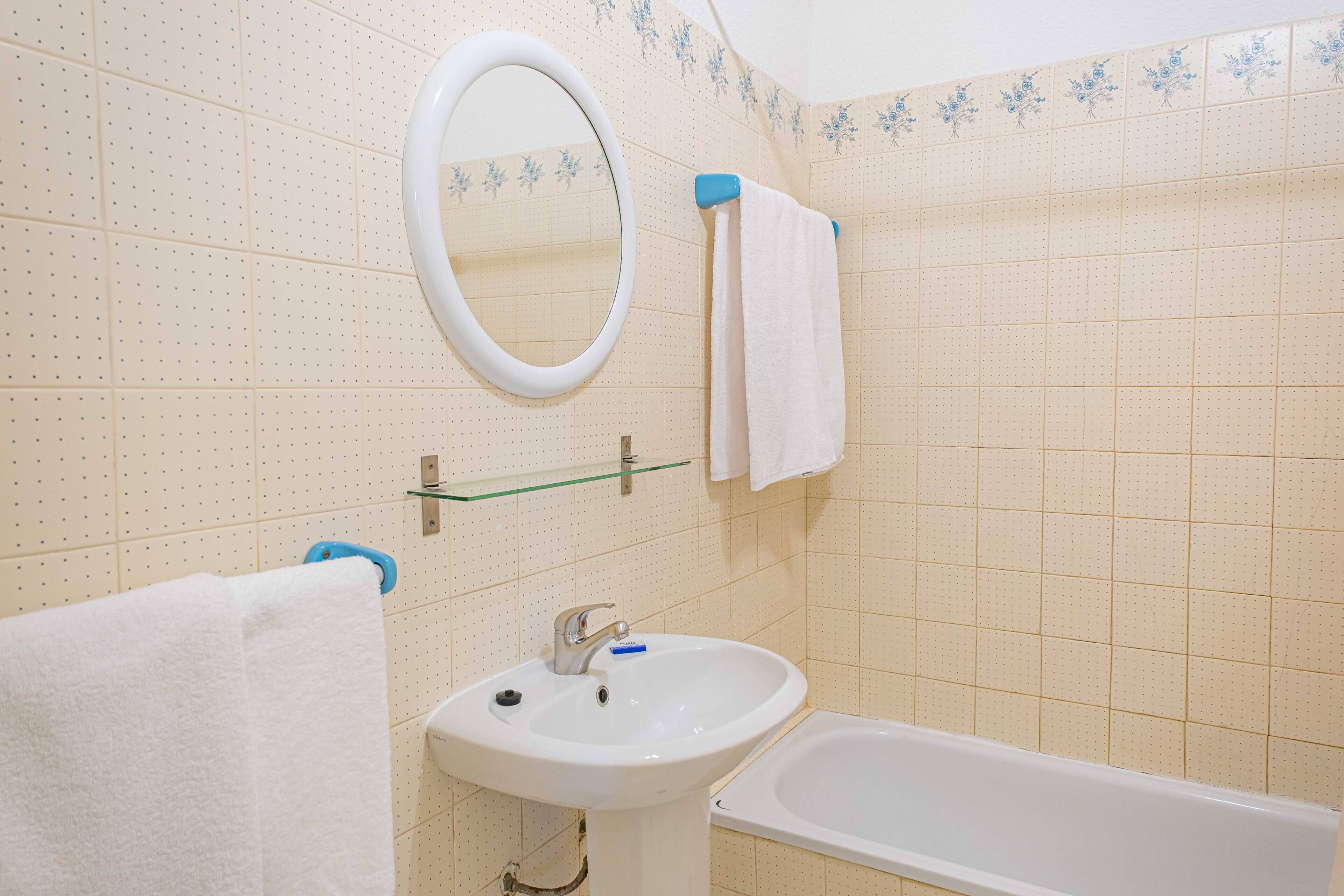 Une salle de bain avec un lavabo blanc, un miroir, une baignoire et un porte-serviettes.