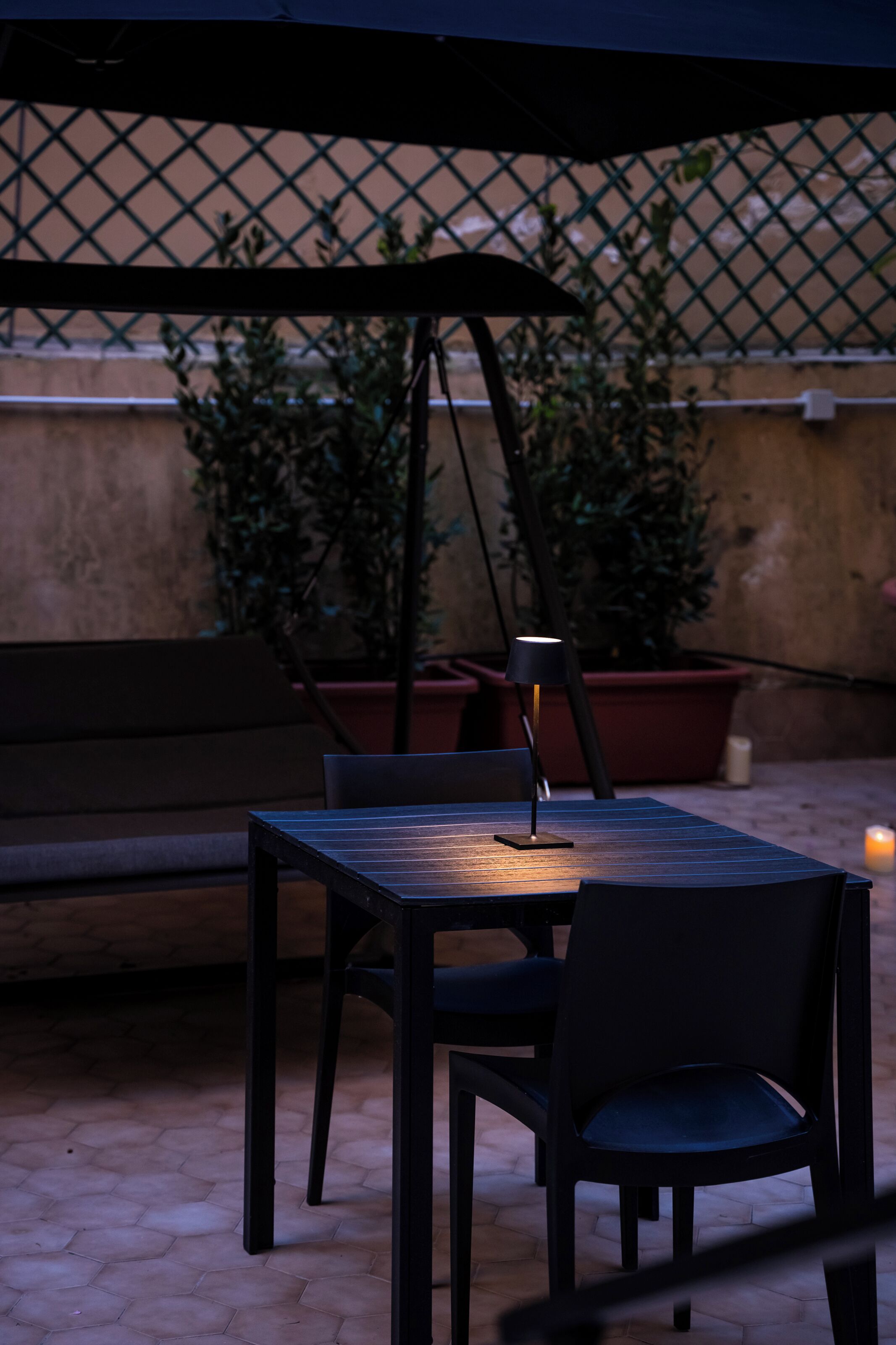 Un espace extérieur aménagé avec une table, des chaises, une lampe et des plantes en pot.