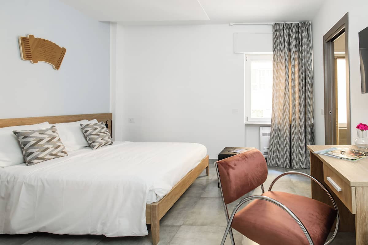 Ein Hotelzimmer mit Bett, Schreibtisch, Stuhl und einem Fenster mit Vorhängen.