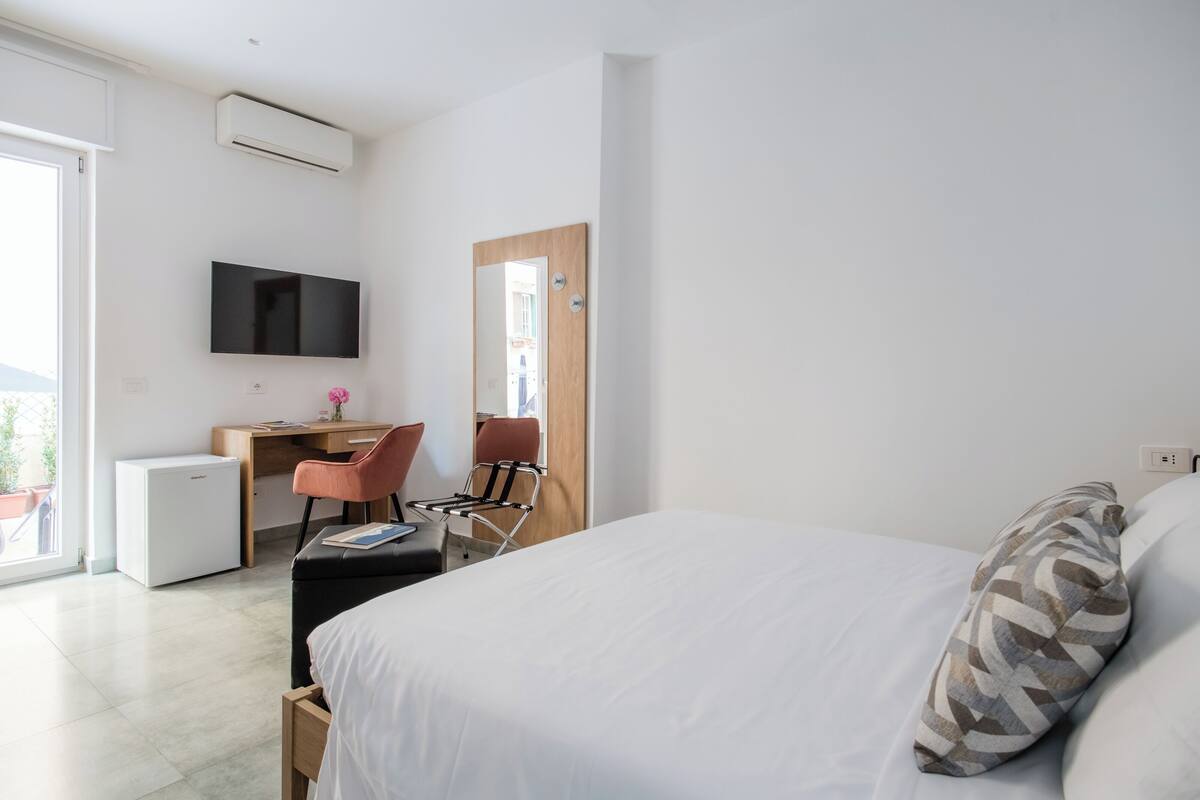 Ein modernes Hotelzimmer mit einem Bett, einem Schreibtisch mit Stuhl, einem Fernseher und einem kleinen Kühlschrank.