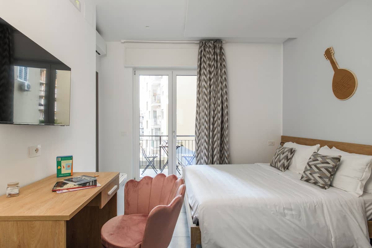 Ein Hotelzimmer mit Bett, Schreibtisch, Stuhl, einer Gitarren-Wanddekoration und Blick auf den Außenbalkon.