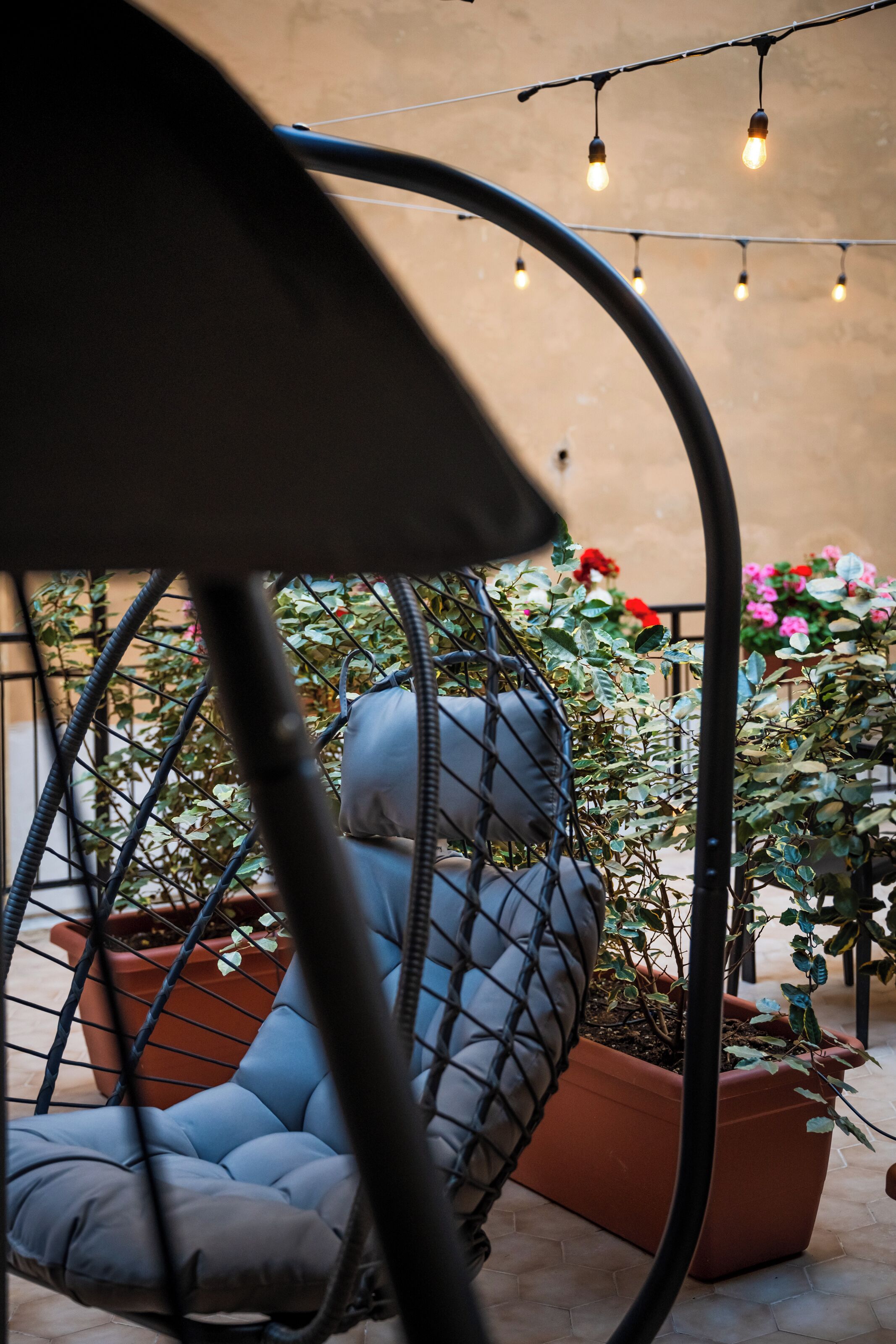 A hanging chair with cushions, surrounded by potted plants and string lights.