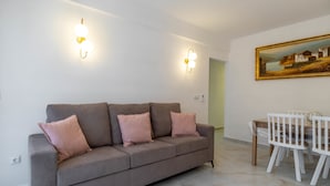 A modern living room with a grey sofa, white walls, and a dining area with a wooden table and white chairs.