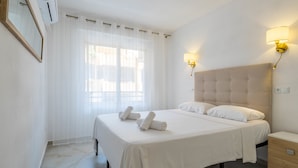 A hotel room with a bed, bedside tables, a wall-mounted air conditioner, and a window with curtains.