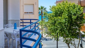 A balcony with white chairs and a blue railing, overlooking a clear blue sky and a tree.