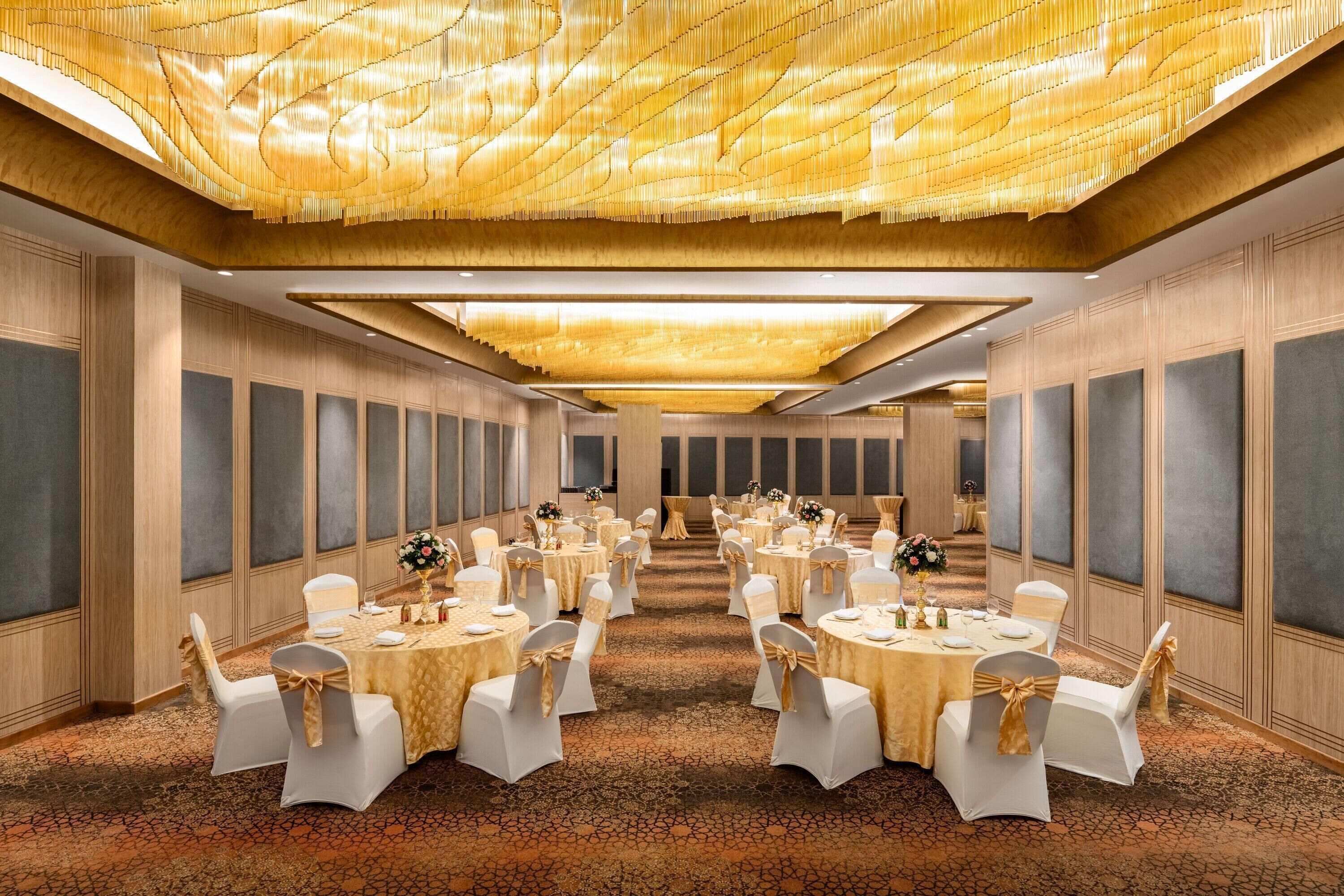 A banquet hall with round tables, white chairs, and a patterned carpet.