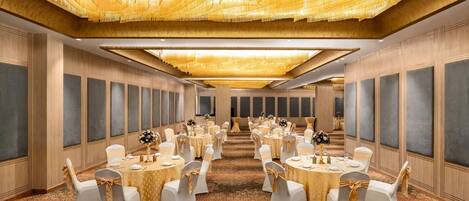 A banquet hall with round tables, white chairs, and a patterned carpet.