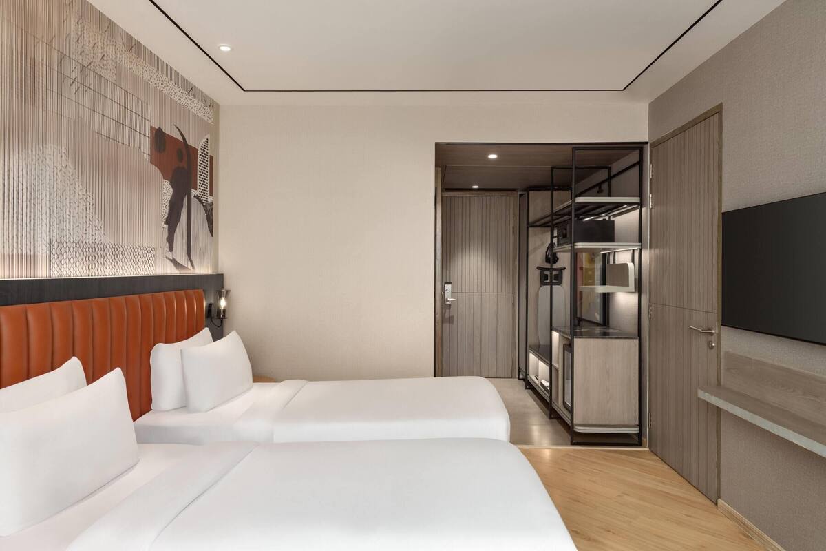 A hotel room with two beds, a TV, a wardrobe, and a hallway leading to a bathroom.
