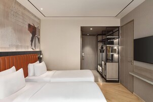 Habitación de hotel con dos camas, televisión, armario y un pasillo que lleva a un baño.