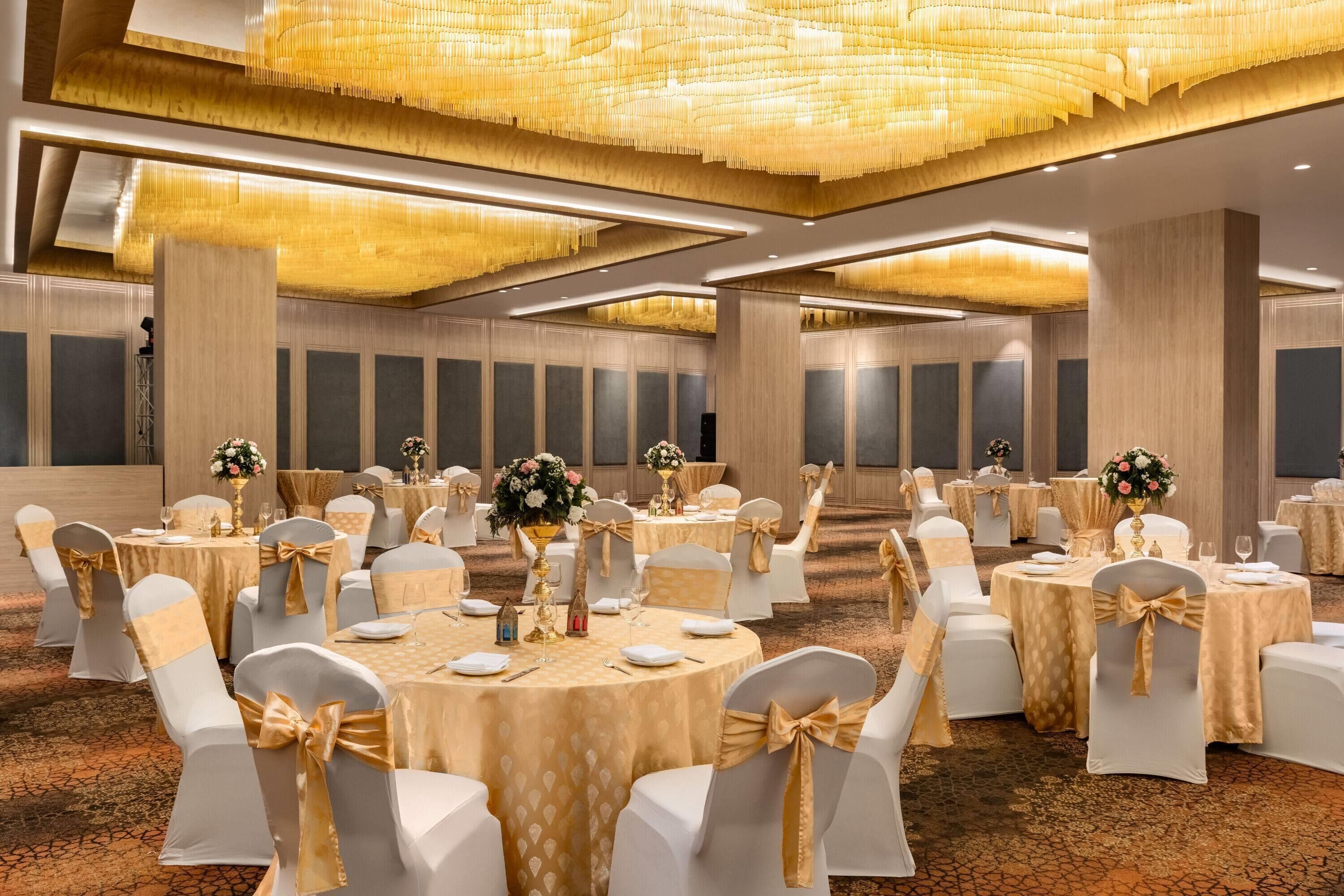 A banquet hall with round tables, white chairs with gold sashes, and a chandelier.