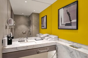 Un baño moderno con tocador de mármol, un espejo grande, una pared de acento amarilla y una obra de arte enmarcada.