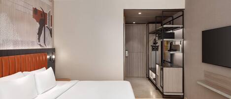 A modern hotel room with a large bed, a TV mounted on the wall, a walk-in closet, and a hallway leading to a bathroom.