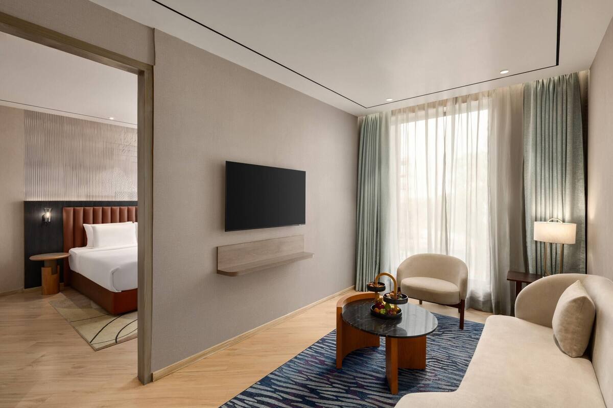 A modern hotel room with a bed, a flat-screen TV, a coffee table, a sofa, and a lamp.