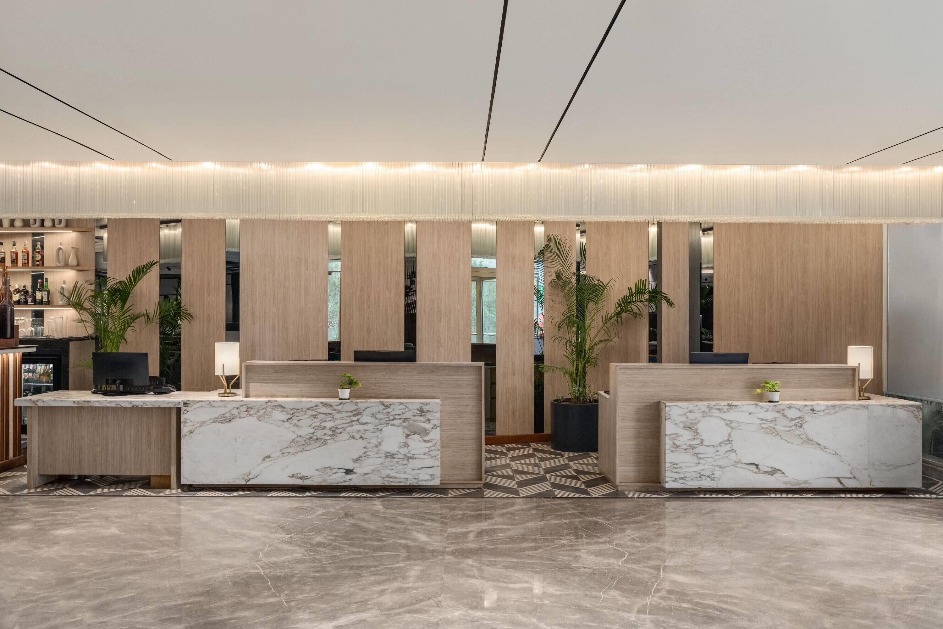 A modern reception area with marble reception desks, wooden paneling, and potted plants.
