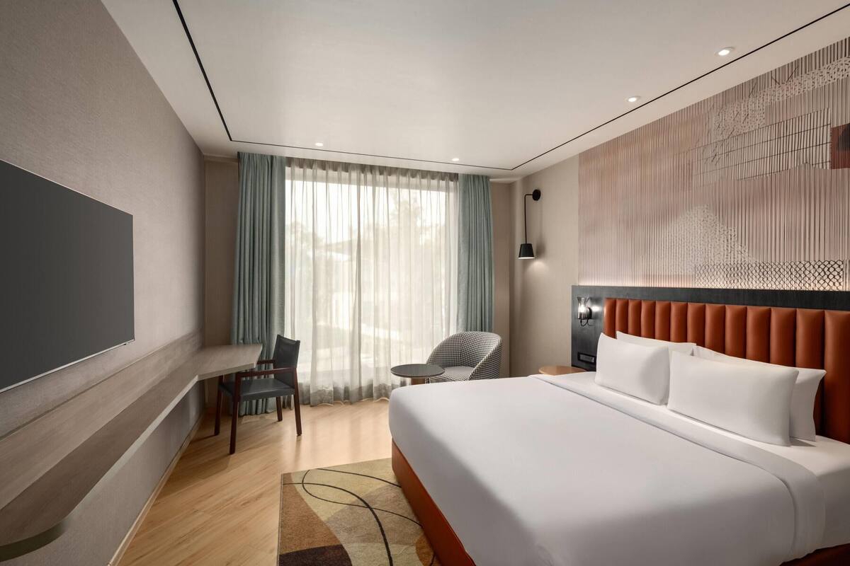 A hotel room with a large bed, a desk, a chair, and a small table.