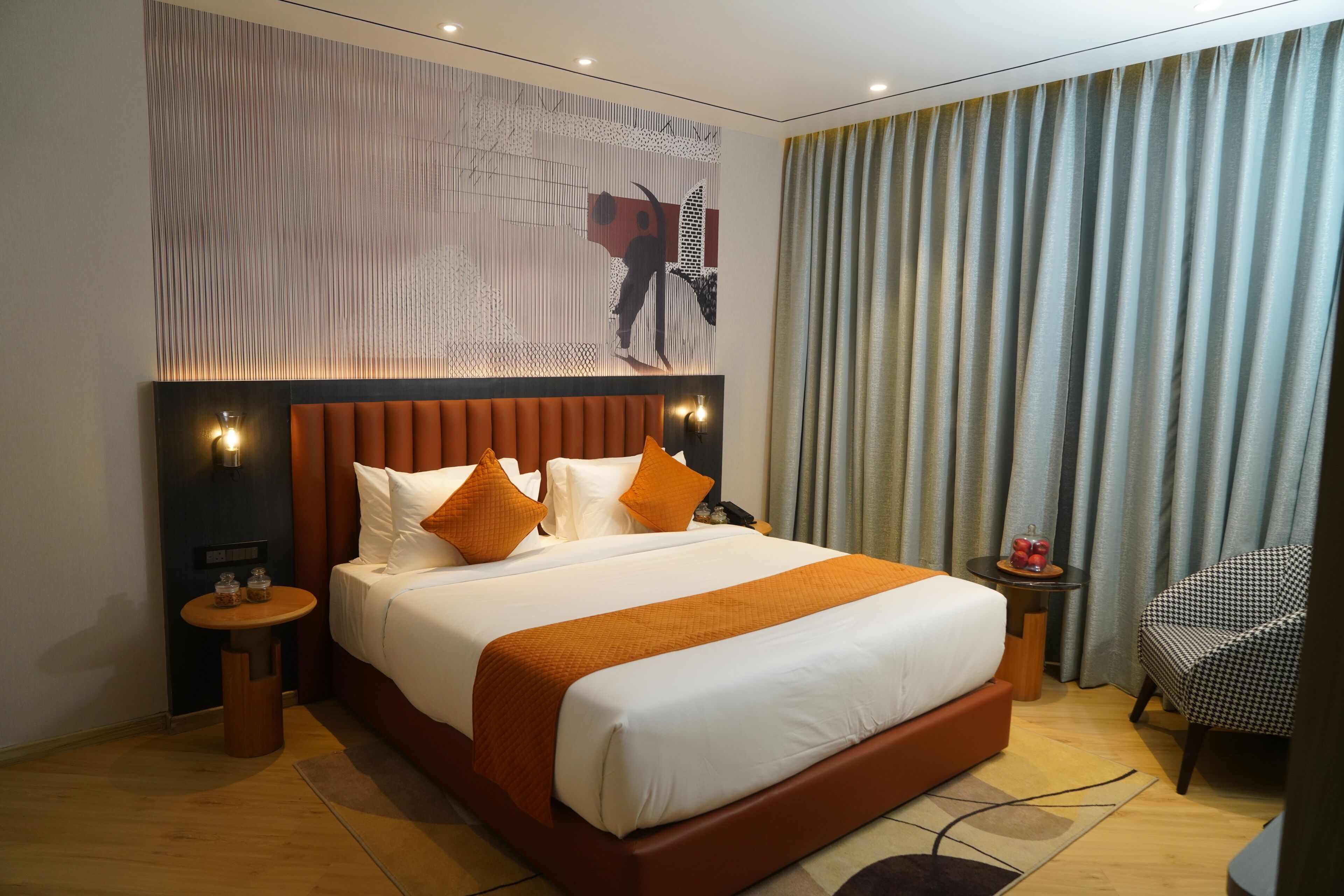 Habitación de hotel con una cama grande, cabecera, mesita de noche, una silla y una pared con diseño decorativo.