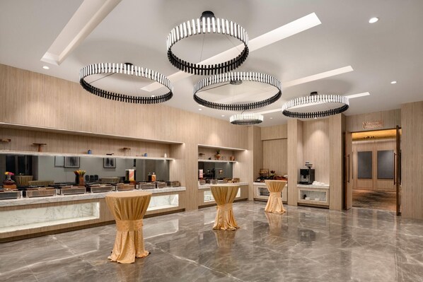 Un moderno vestíbulo de hotel con mostradores de mármol, mesas con adornos dorados y candelabros circulares.