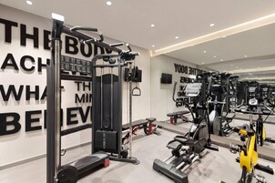 Un gimnasio con equipo de ejercicio, una pared con texto motivacional y un espejo que refleja el equipo.