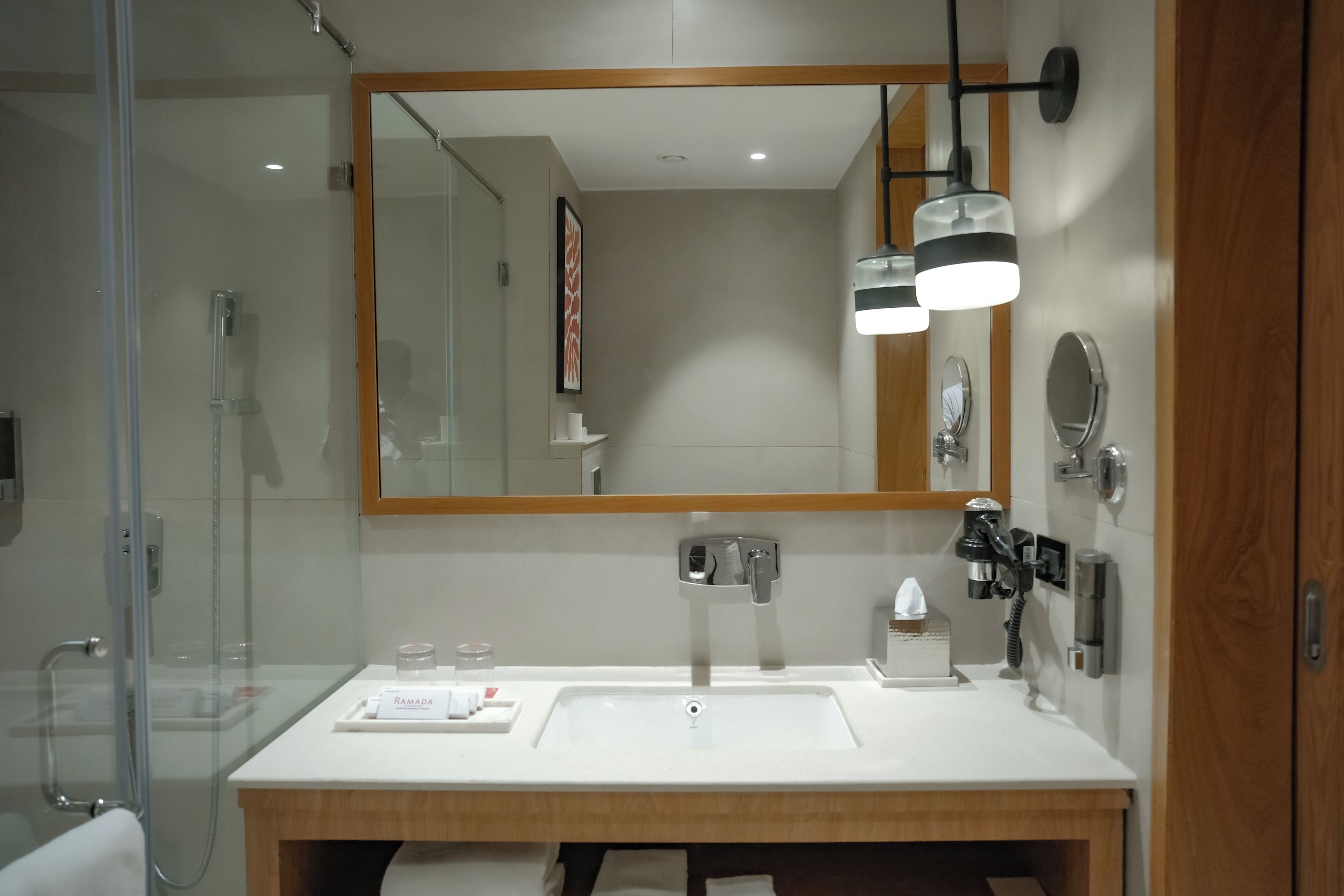 Een moderne badkamer met een douche met glazen wanden, een grote spiegel en een witte wasbak.