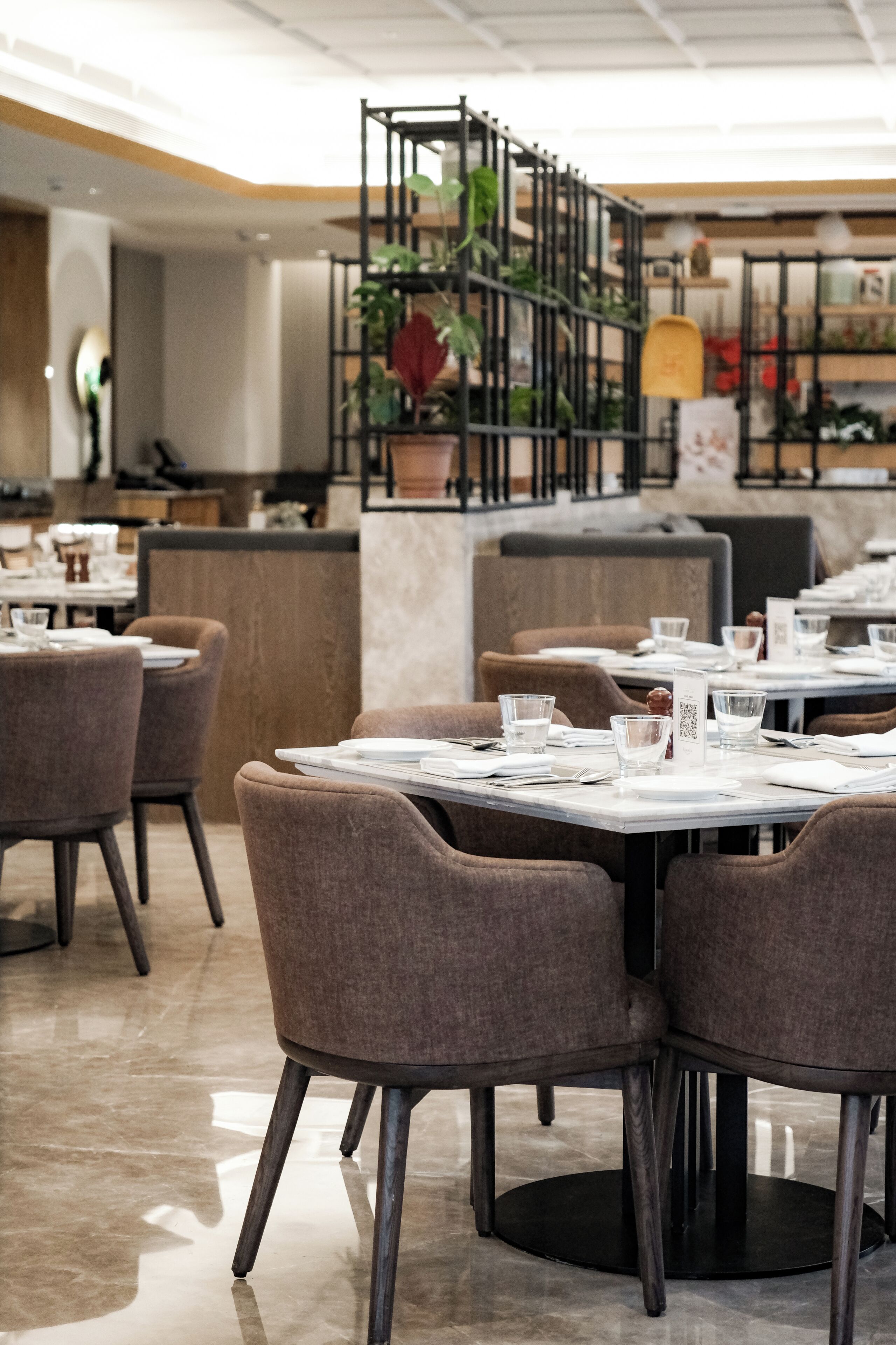 A restaurant with round tables, brown chairs, and a central plant display.