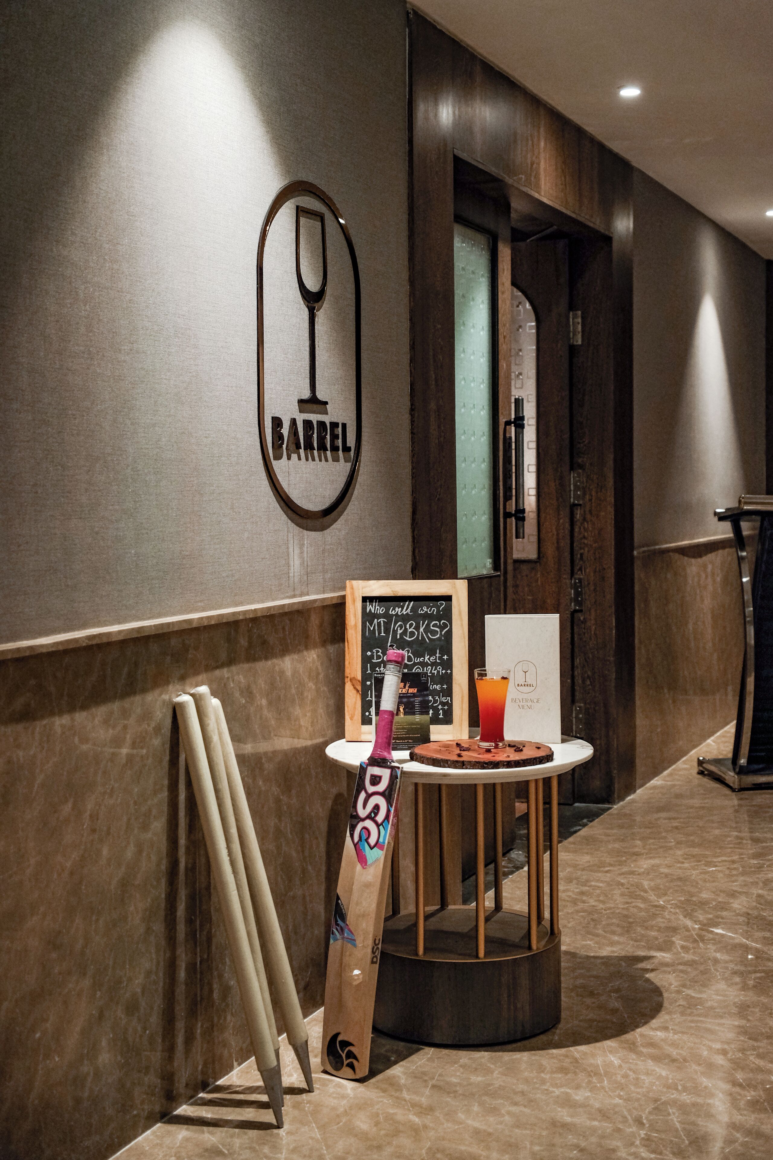 Un coin bar avec un tableau noir servant de panneau, un tabouret en bois et une batte appuyée contre le mur.