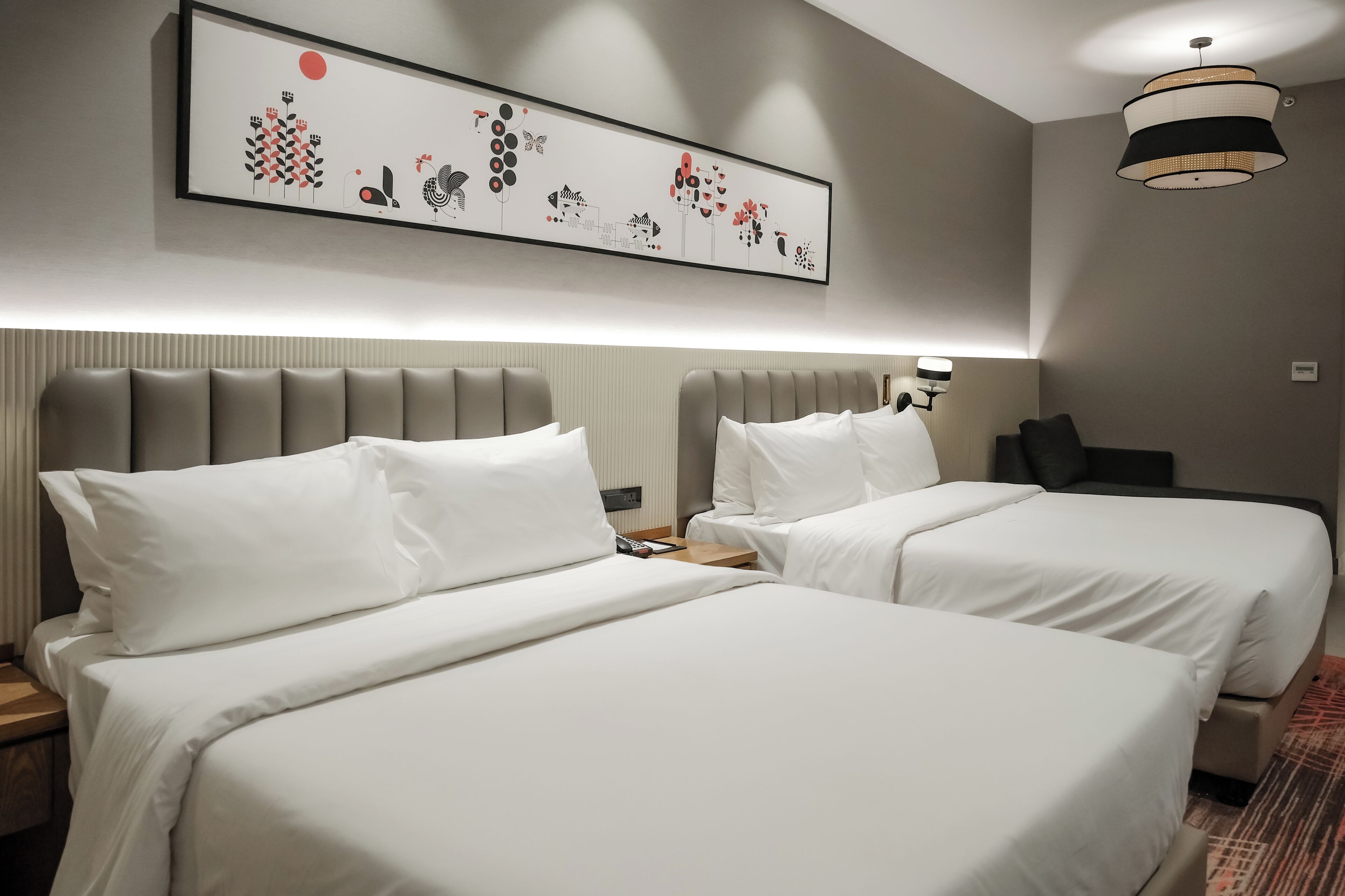 Habitación de hotel con dos camas, cabecero, una obra de arte colgada en la pared, mesita de noche y lámpara.