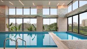 A modern indoor swimming pool with large windows, a clear view of the surrounding greenery, and a tiled floor. - Ramada by Wyndham Ranchi (Ranchi)