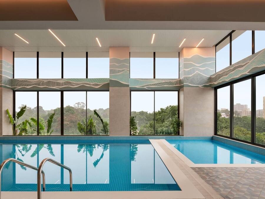 A modern indoor swimming pool with large windows, a clear view of the surrounding greenery, and a tiled floor.