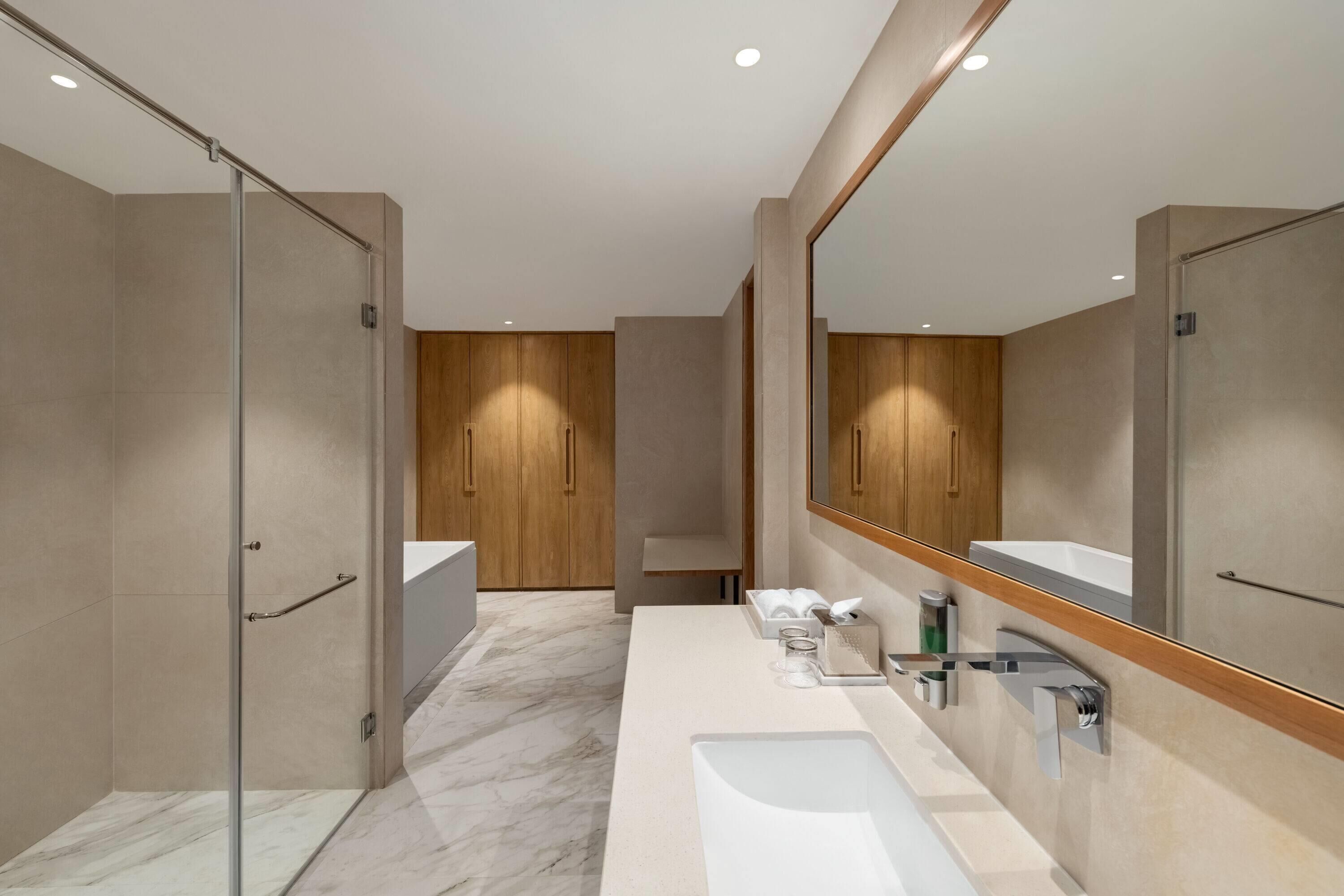 A modern bathroom with a glass shower enclosure, a large mirror, and a marble floor.