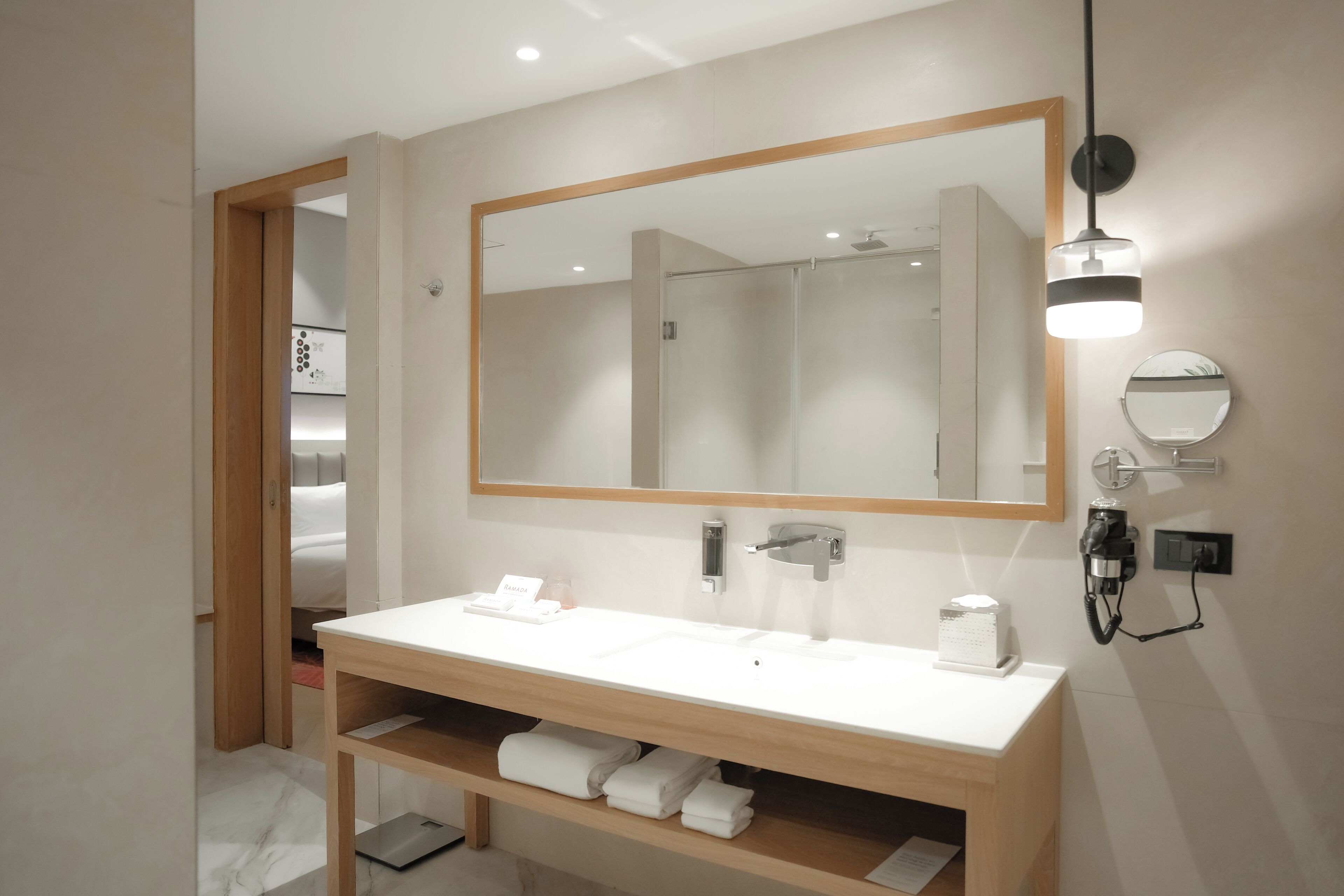 Un baño moderno con un espejo grande, lavamanos blanco, toallero y cabezal de ducha de mano.