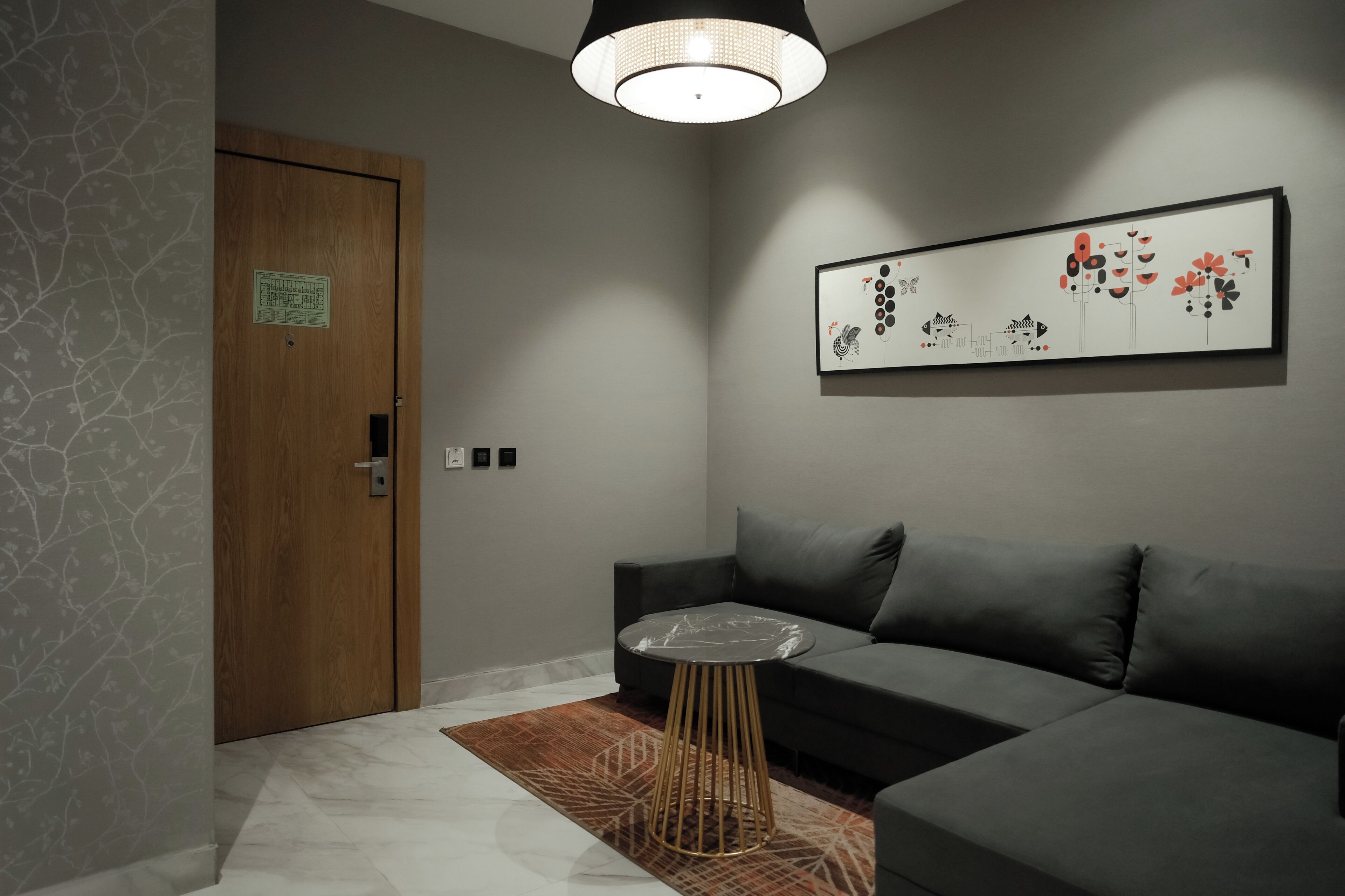 Un salon moderne comprenant un canapé, une table ronde, un tapis à motifs, une porte en bois et une œuvre d’art accrochée au mur.