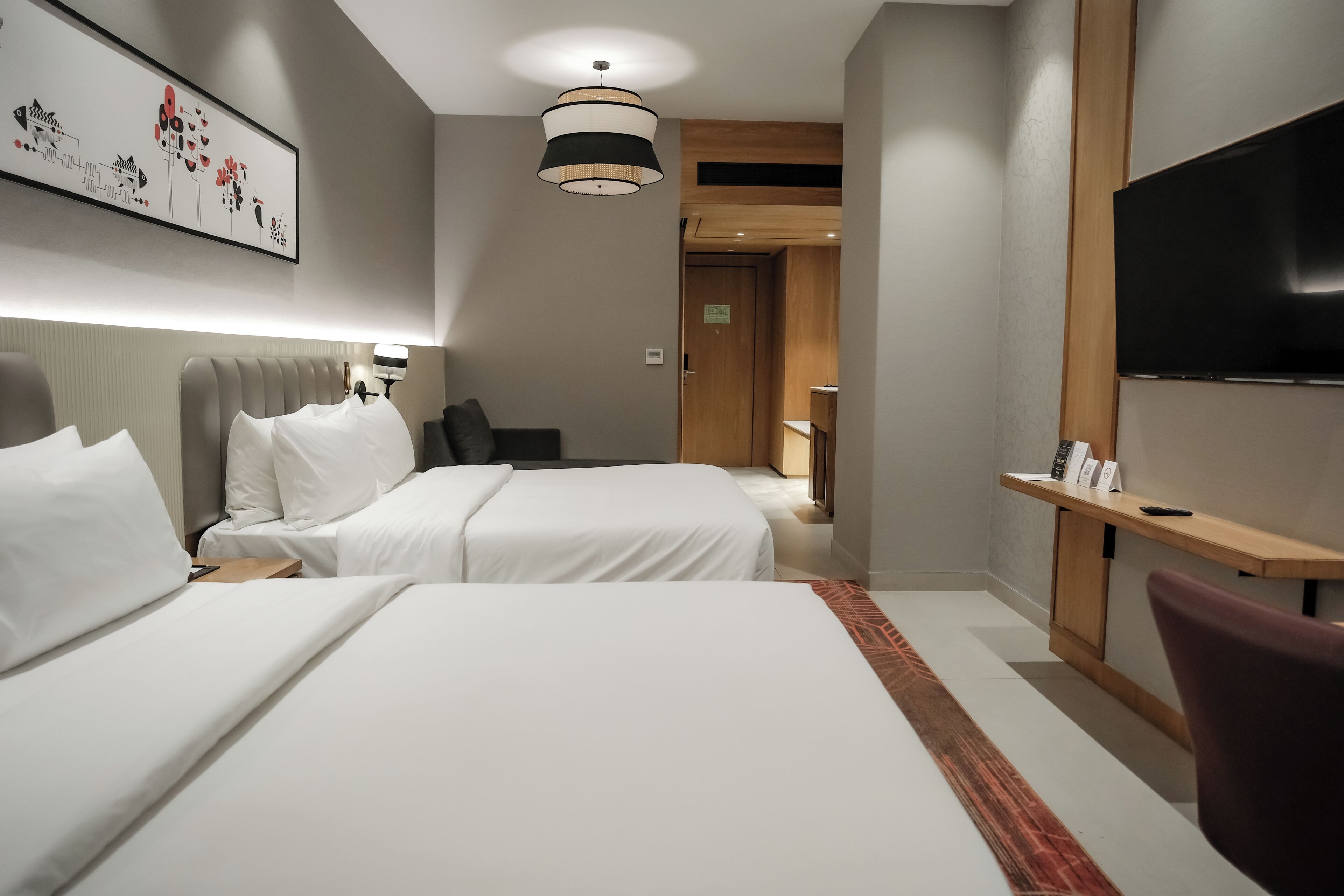 A hotel room with two beds, a TV, a desk, and a painting on the wall.