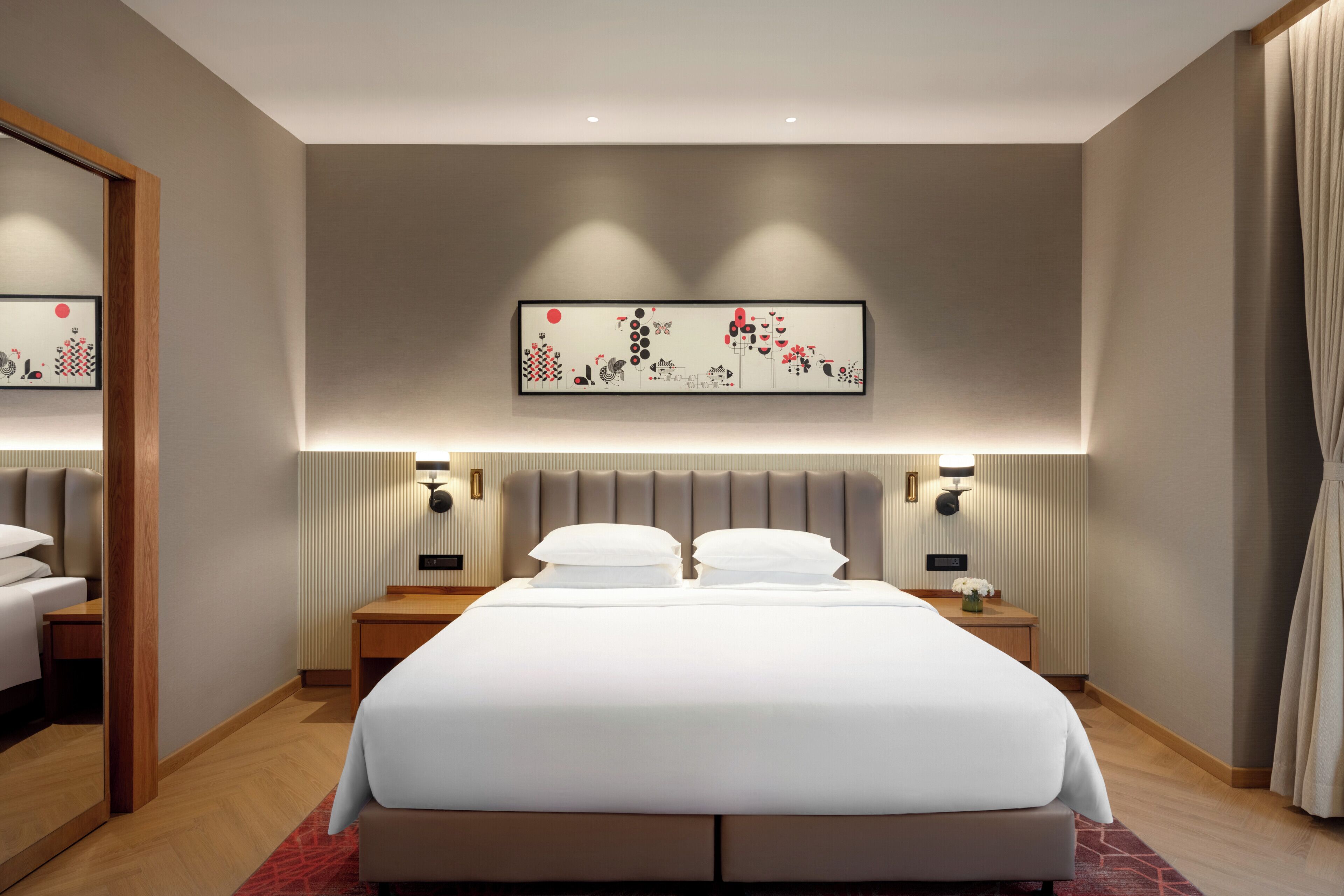 A modern hotel room with a large bed, bedside tables, and a wall-mounted artwork.