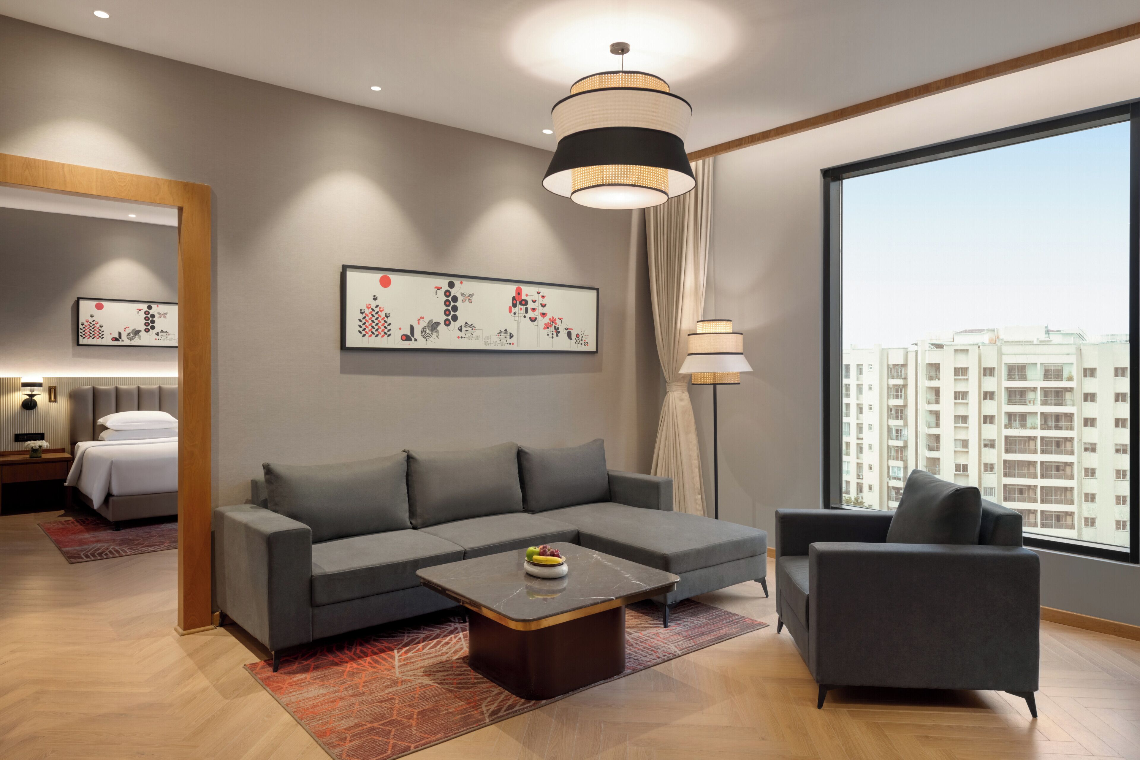 A modern living room with a grey sofa, a coffee table, and a large window offering a city view.