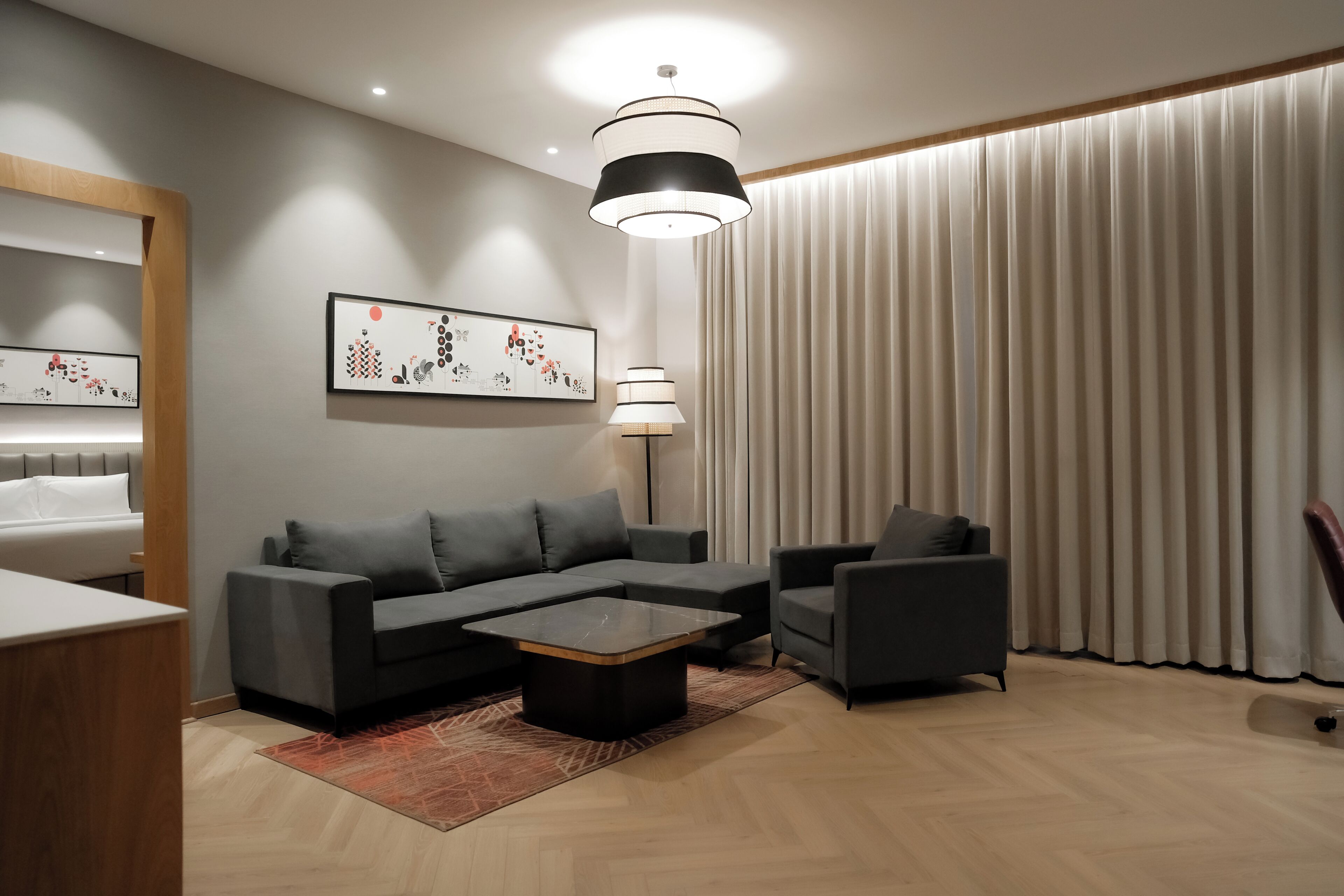 A modern living room with a sectional sofa, a coffee table, a side table, a lamp, and a large window with curtains.