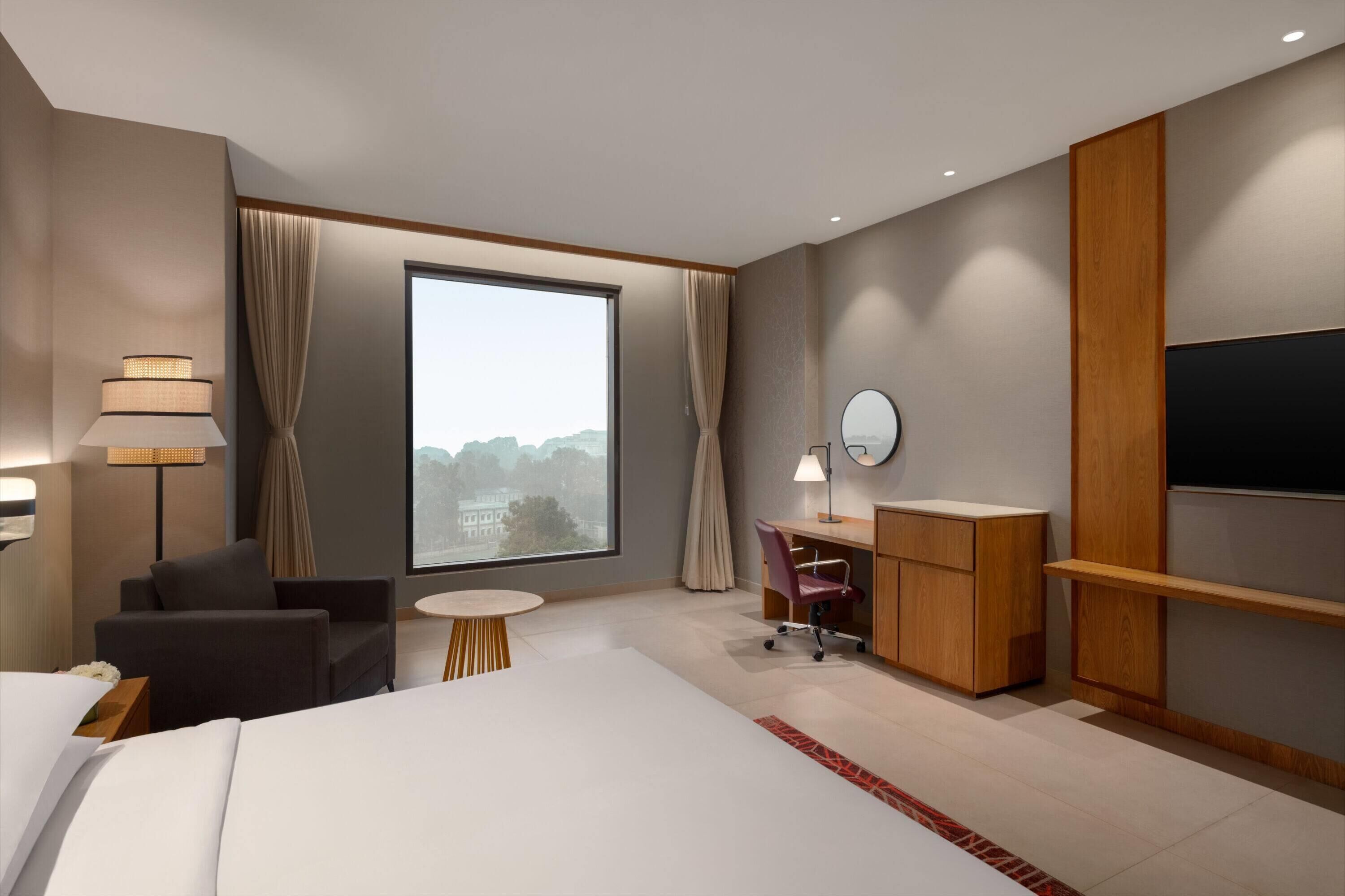 Una moderna camera d'albergo con un letto grande, una scrivania, una sedia, un televisore e una finestra con tende.