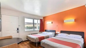 Ein Hotelzimmer mit zwei Betten, einem Schreibtisch und einem Fenster mit Blick nach außen.