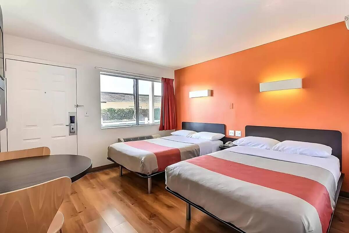 Habitación de hotel con dos camas, un escritorio y ventana con vistas al exterior.