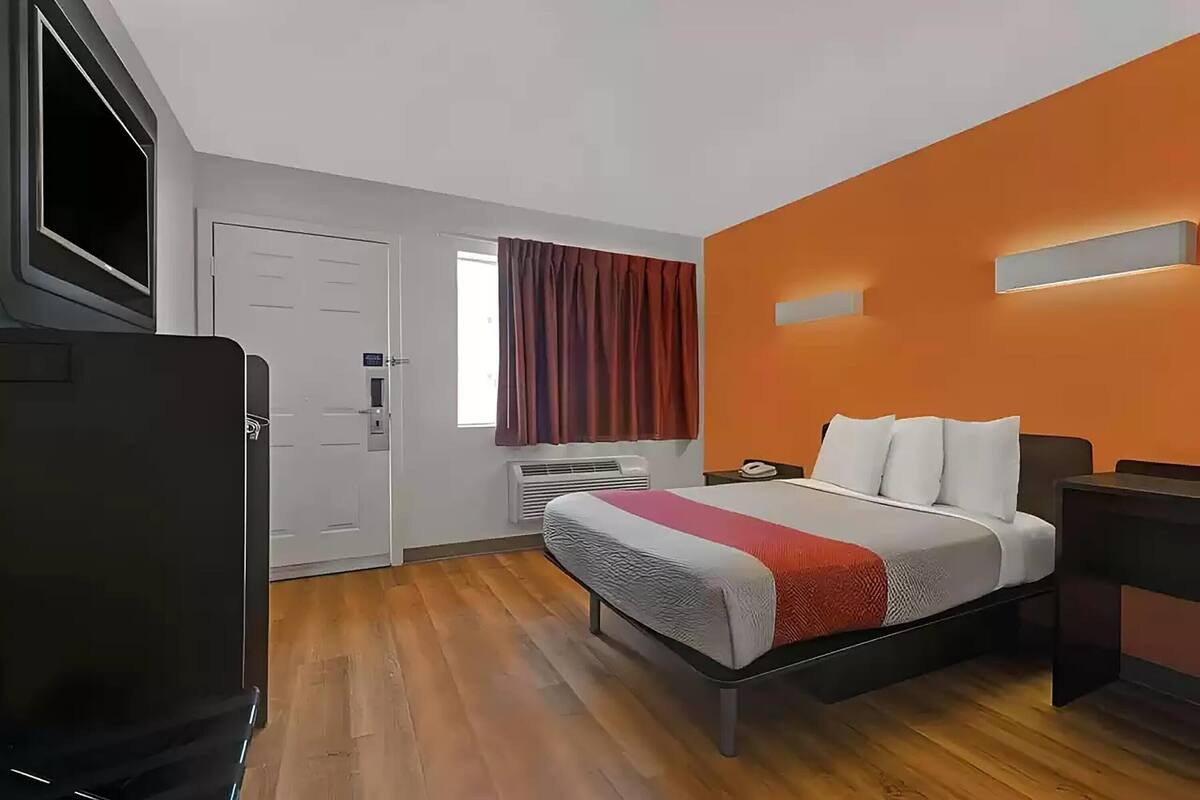 Una habitación de hotel con una cama, televisor, escritorio y aire acondicionado.