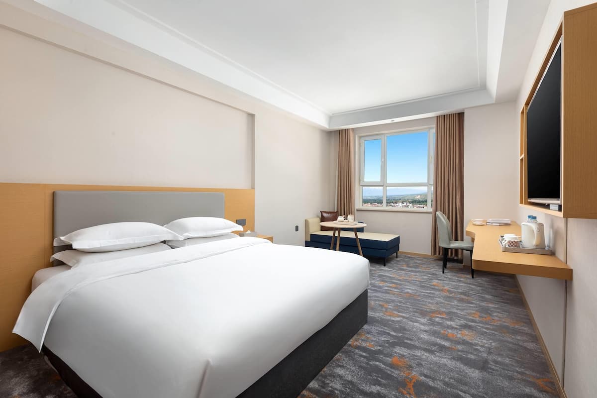 Quarto de hotel com uma cama grande, uma escrivaninha, uma cadeira e vista para a cidade.