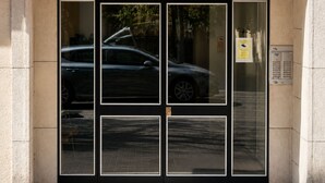 Entrada de un edificio con puerta de cristal, cartel de estacionamiento y un cuadro eléctrico.