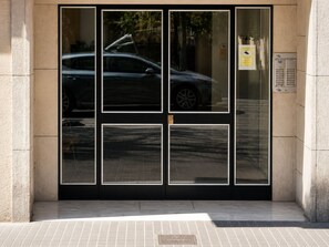 Entrada d'un edifici amb una porta de vidre, un senyal de pàrquing i una caixa de subministraments.