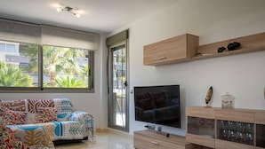 A modern living room with a sofa, TV, wooden cabinet, and large windows. - Peaceful ground floor with private garden and terrace (Torredembarra)