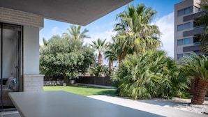 A modern outdoor patio with a flat table and chairs, surrounded by lush greenery and palm trees. - Peaceful ground floor with private garden and terrace (Torredembarra)