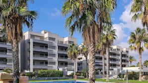A modern hotel with multiple floors, a swimming pool, and palm trees. - Peaceful ground floor with private garden and terrace (Torredembarra)