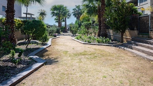 A pathway flanked by palm trees and small shrubs, leading to a building with multiple balconies. - Peaceful ground floor with private garden and terrace (Torredembarra)