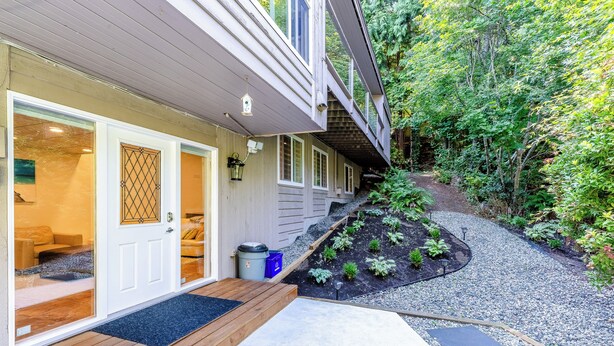 A house with a wooden deck, a front door, and a garden with a gravel path.