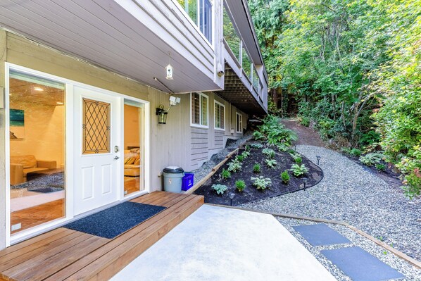 A house with a wooden deck, a front door, and a garden with a gravel path.