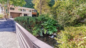 A house with a covered garage, a small pond, and dense greenery.